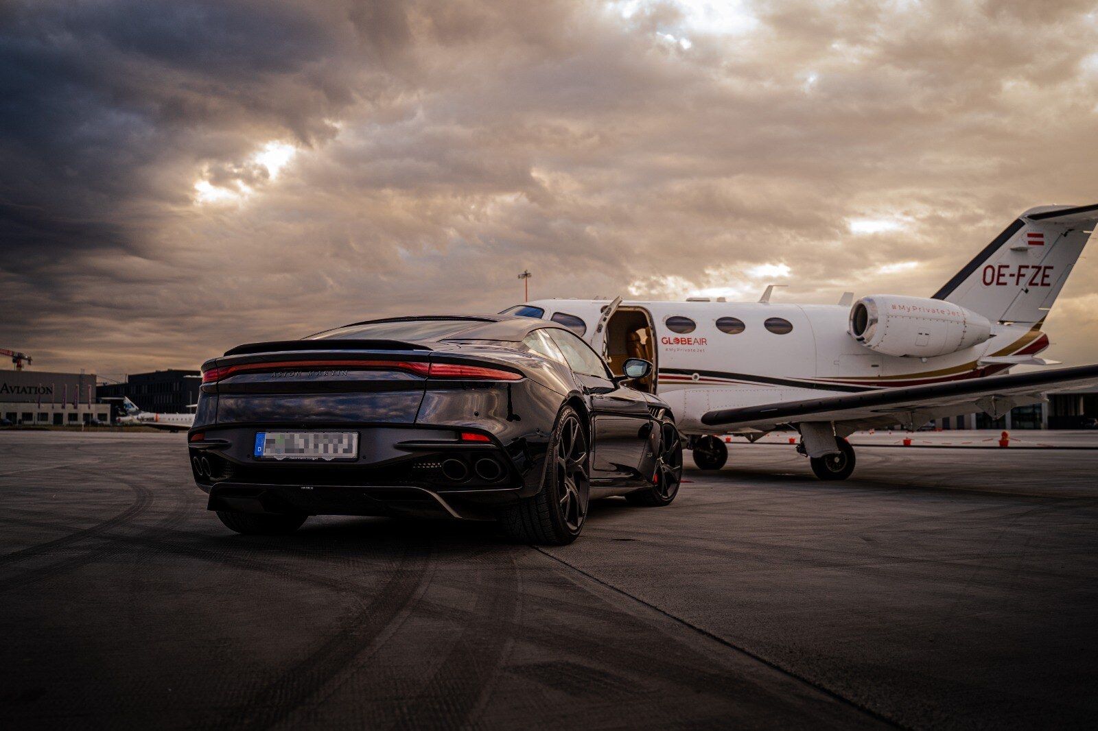 Schwarzer Sportwagen vor einem Privatjet in der Abenddämmerung